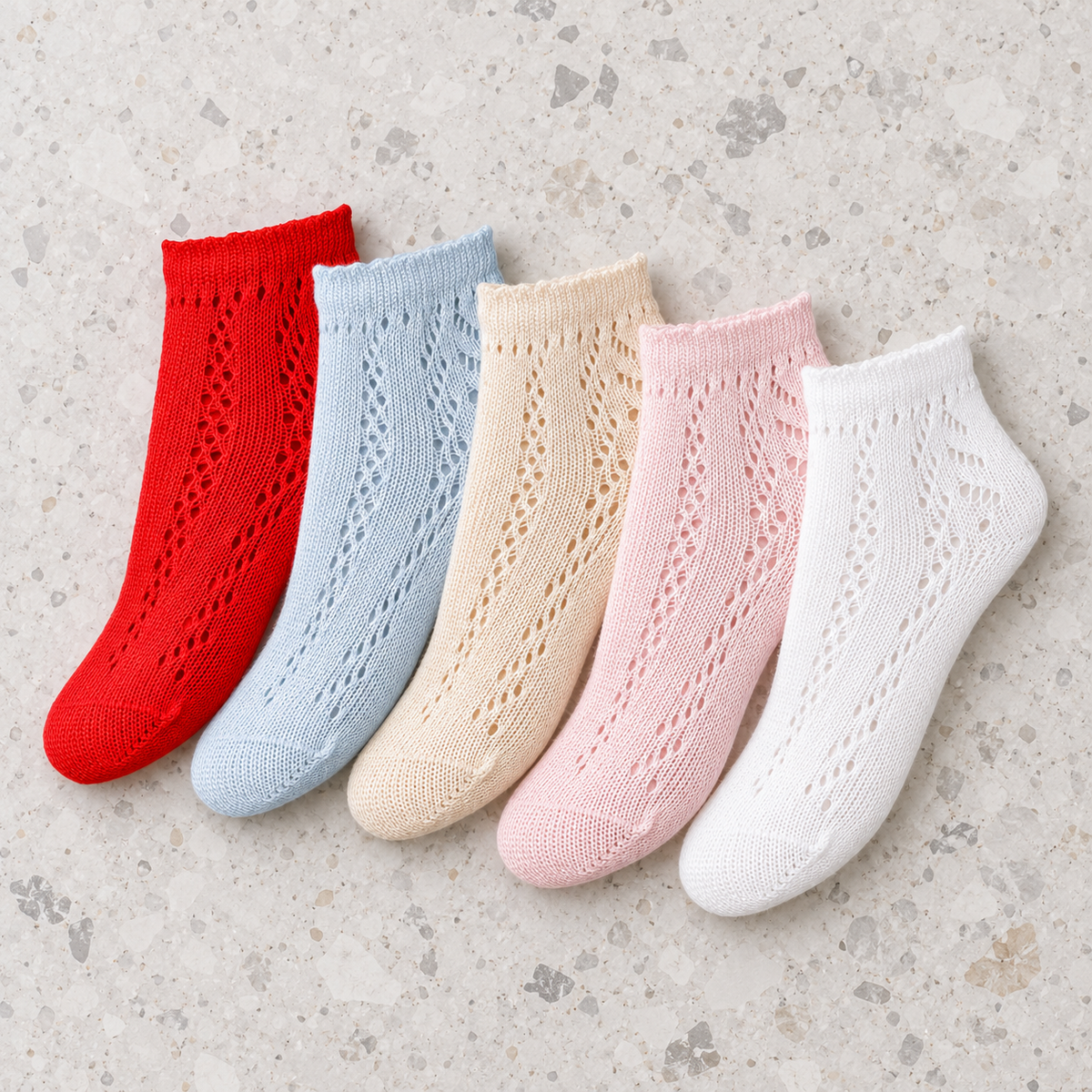 Miranda Perle girls openwork ankle socks in red, pale blue, cream, pale pink and white arranged on grey terrazzo marble