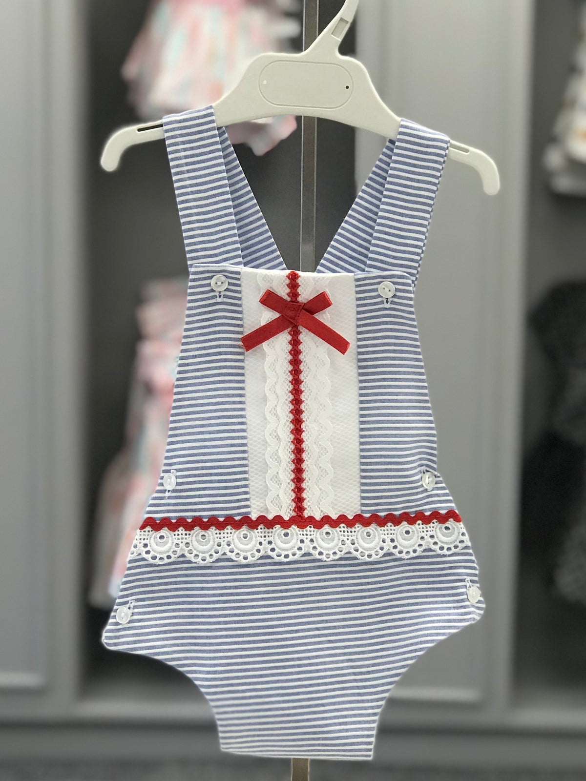 Eva Class Nati girls blue and white striped romper with white lace panel, red satin bow and crossover shoulder straps