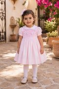 Little girl in Spain wearing Naxos Alma hand smocked pink dress.