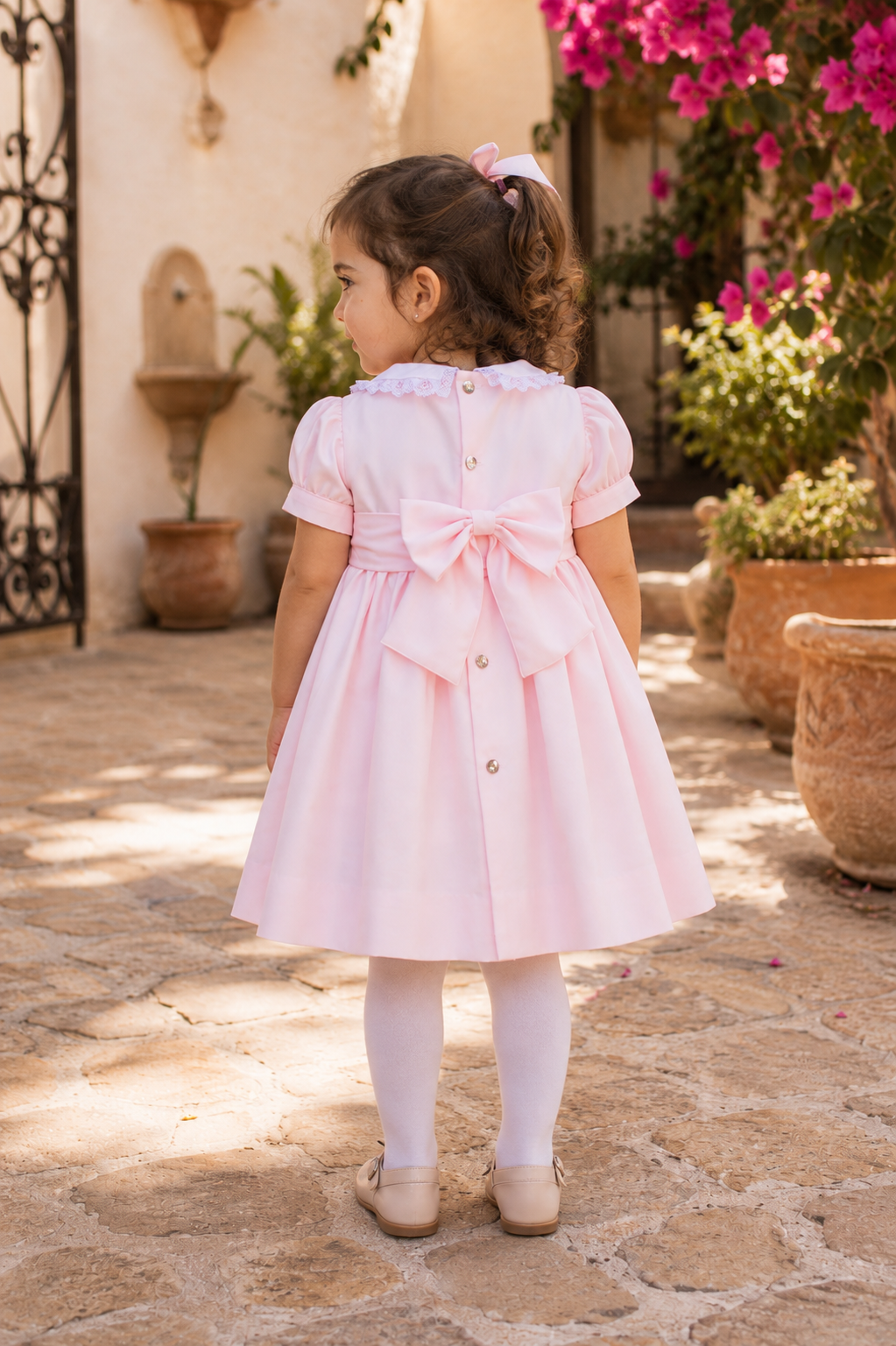 Little girl wearing Naxos Alma pink hand smocked dress showing the bow on the back