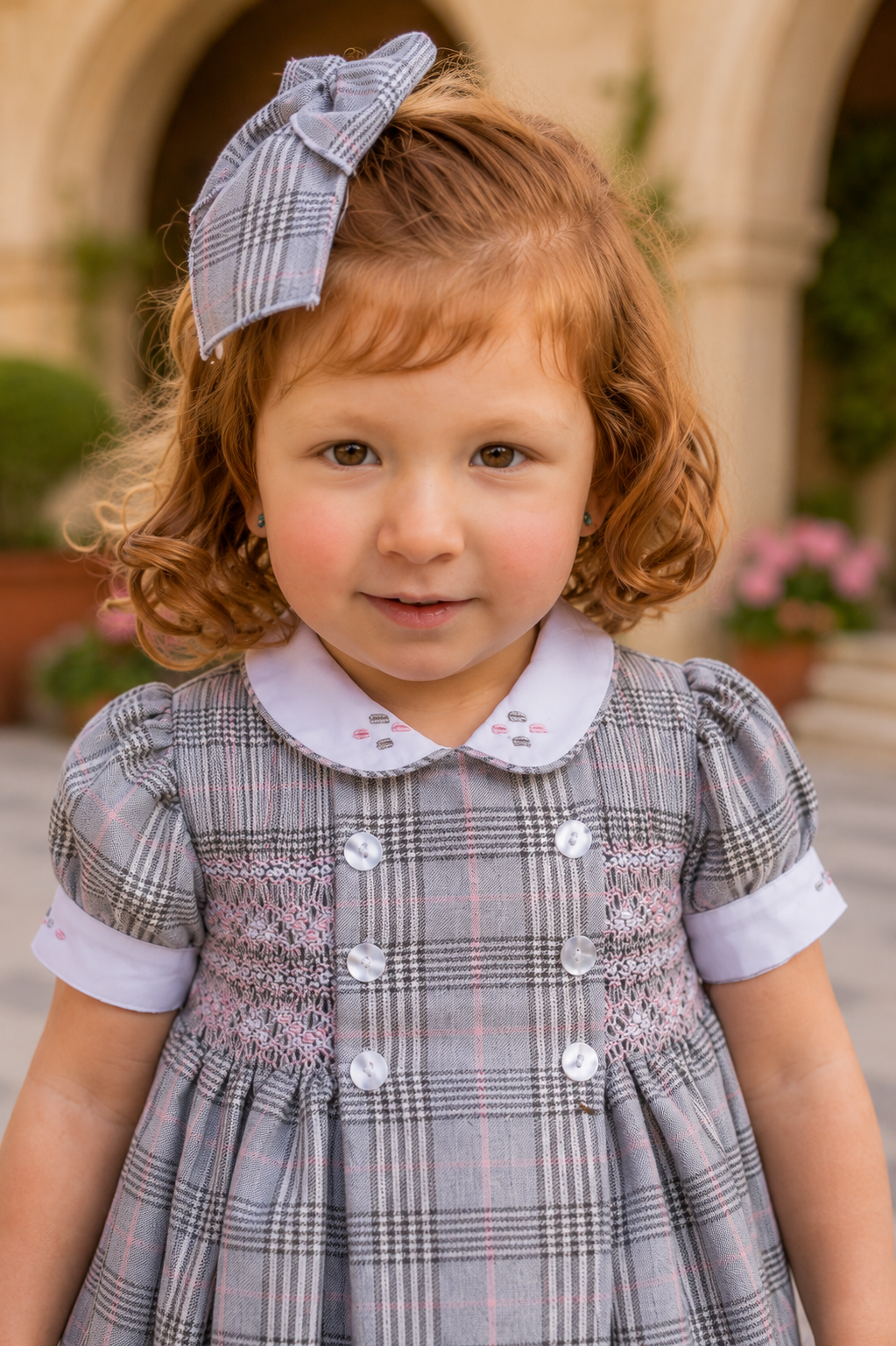 Naxos Laura grey check girls dress featuring intricate pink hand smocking and embroidered white collar.
