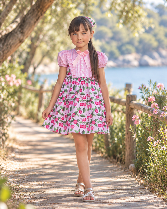 Rochy Cherry girls pink cherry print dress with gingham bodice, puff sleeves and pink bow in a sunny lakeside setting