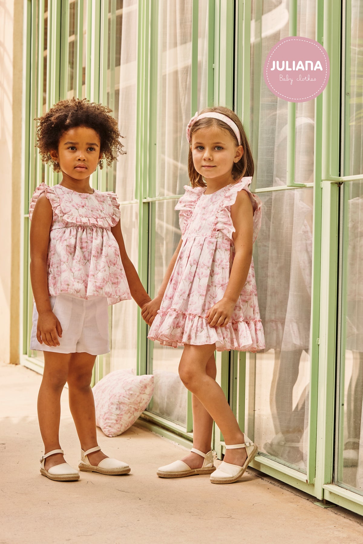 Girls wearing coordinating Juliana Caramelo pink floral dress and short set in a glasshouse.