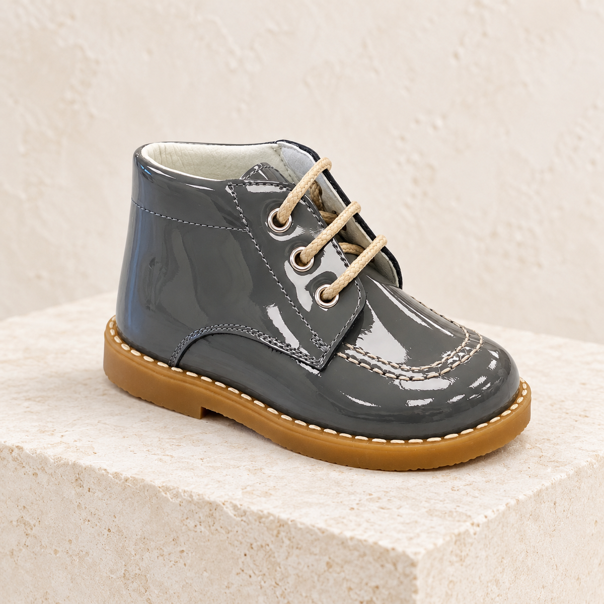 Andanines grey patent leather boys lace-up boots on a warm ivory studio background