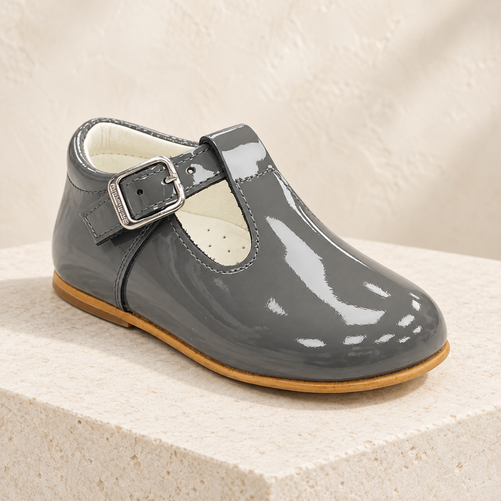 Andanines grey patent leather boys T-bar shoe on a cream stone plinth