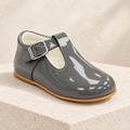 Andanines grey patent leather boys T-bar shoe on a cream stone plinth
