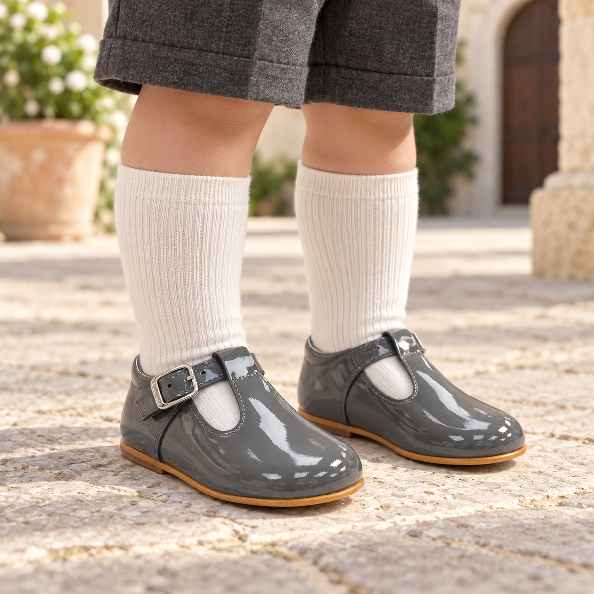 Boy wearing Andanines grey patent leather T-bar shoes with ivory knee-high socks