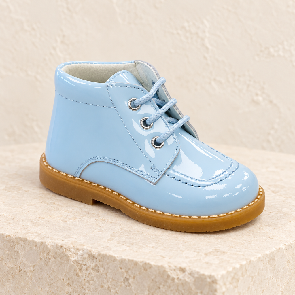 Andanines pale blue patent leather boys lace-up boots on a warm ivory studio background