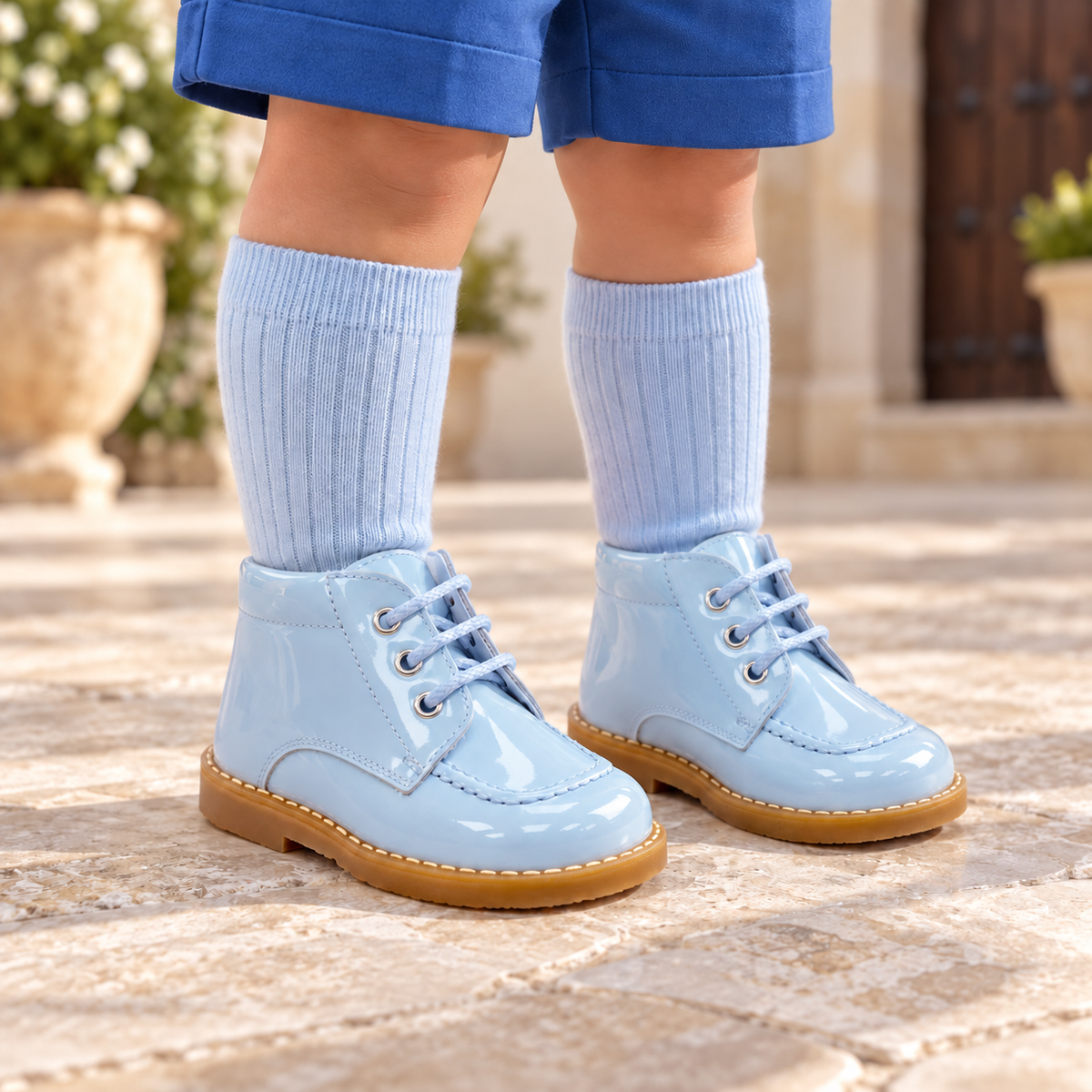 Andanines pale blue patent leather boys lace-up boots worn with blue shorts and coordinating knee-high socks