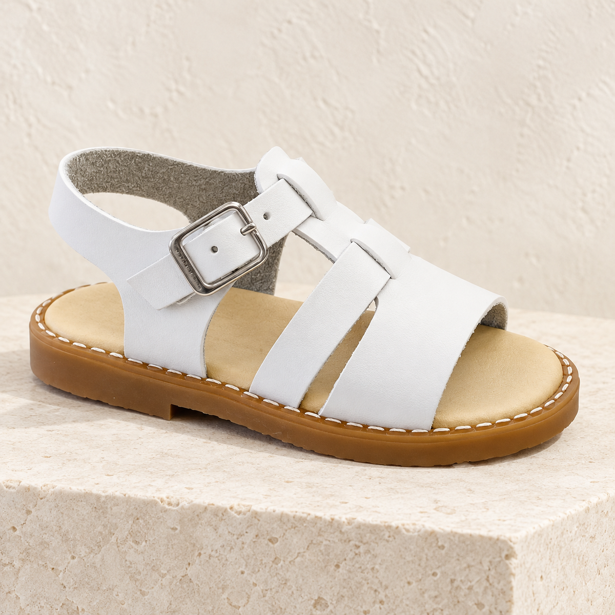 Andanines white leather boys sandal on a cream stone plinth