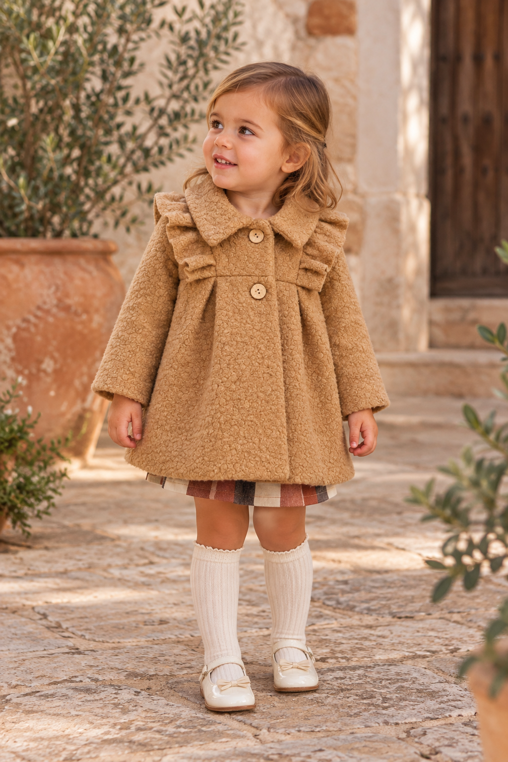 Toddler girl wearing the Babine Calabaza camel bouclé frill coat in a Spanish courtyard