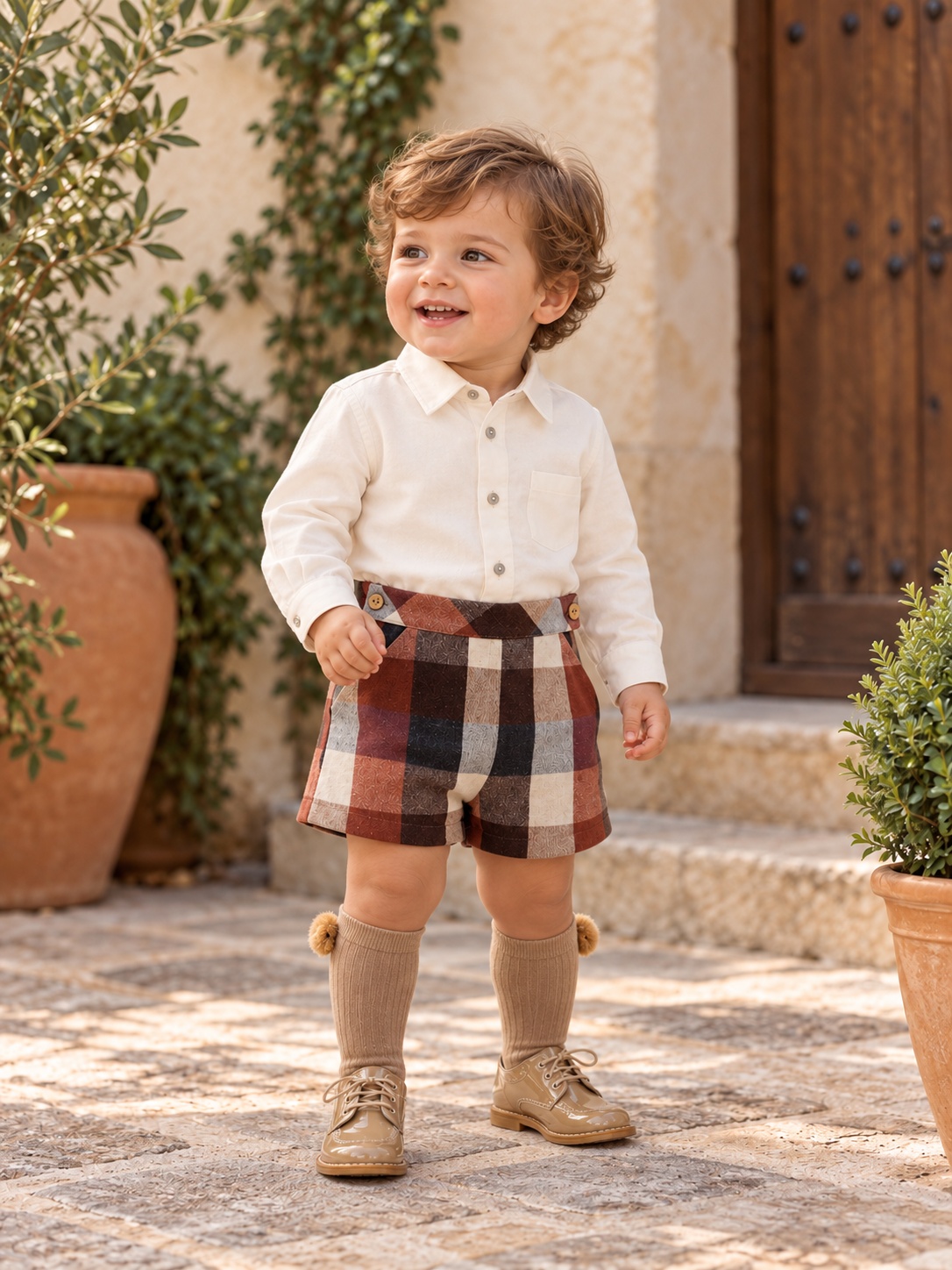 18-month-old boy wearing the Babine Calabaza camel and brown check short set in a Spanish courtyard