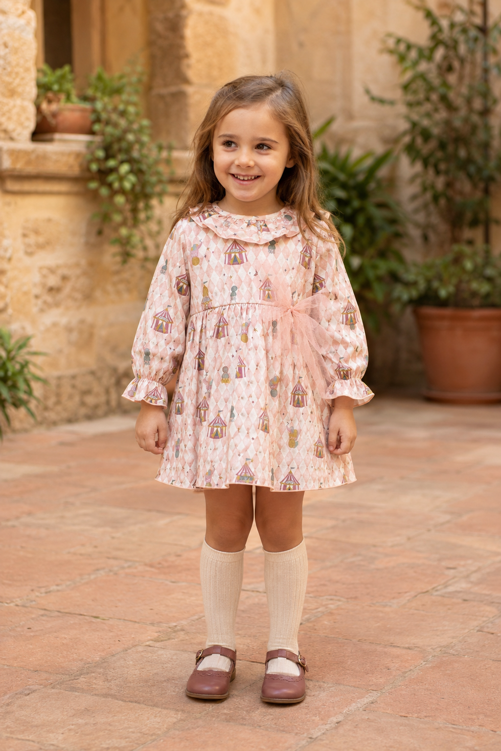 Calamaro Mistral pink circus-print dress on a girl in a Spanish courtyard, front view