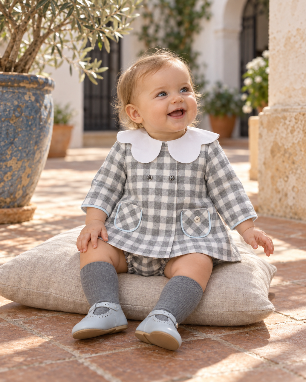 Baby girl wearing the Foque Los Fogones blue-grey check dress and matching knickers in a Spanish courtyard