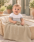 Baby boy with the Juliana Canela beige knitted blanket in a sunlit Spanish courtyard.