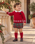 Baby boy wearing Juliana Melodia red knitted jumper and grey tartan jam pant set in a Spanish courtyard