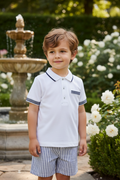 Little boy wearing white polo with navy trim and striped shorts in elegant setting