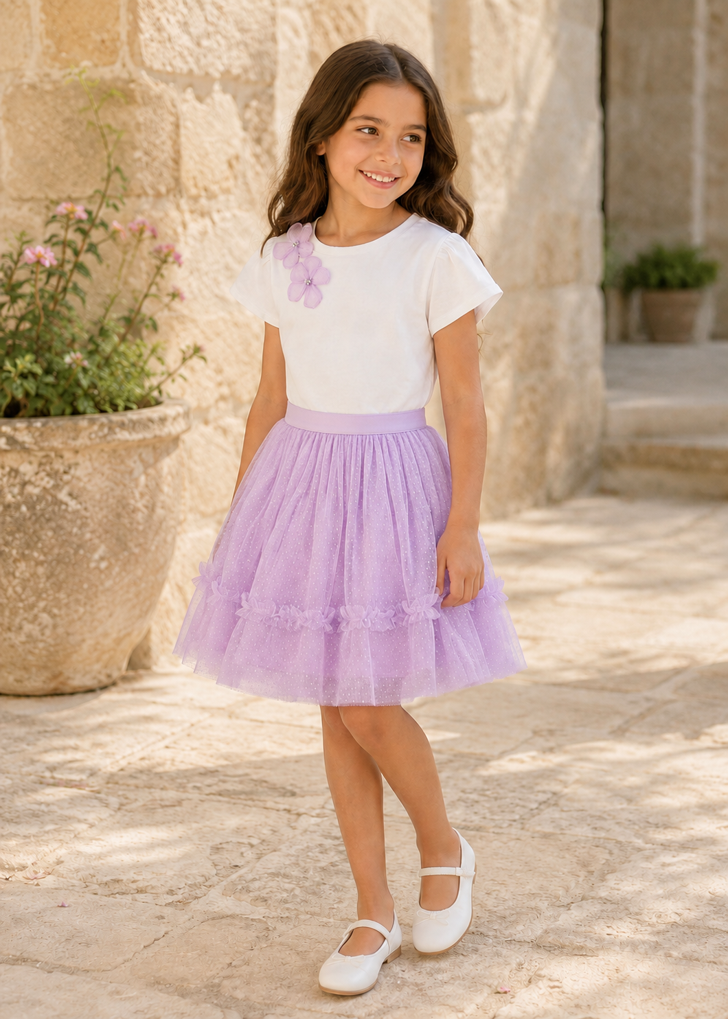 Girl wearing Mayoral ivory flower top and lilac tulle skirt set in a Spanish courtyard