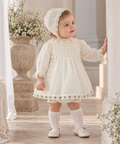Baby girl wearing Miranda Ceremonia cream dress and delicate bonnet in Spanish style