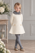 Girl wearing Miranda cream cable knit A-line dress with grey faux fur collar and gold button pocket details