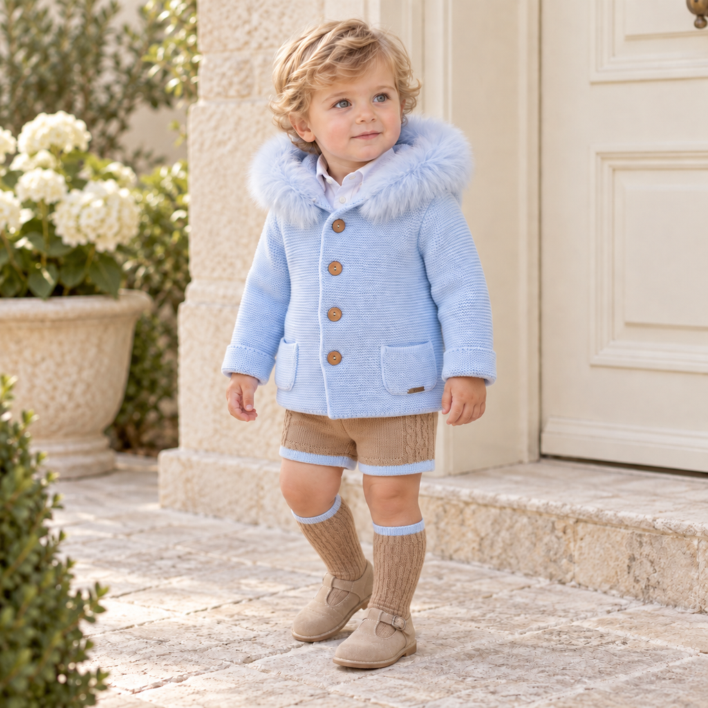 Young boy wearing Rahigo blue knitted coat with fur-trimmed hood, camel knitted shorts and matching socks
