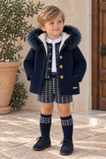 Boy wearing Rahigo navy knitted coat with fur-trimmed hood and cream plush lining, styled with matching navy shorts and knee-high socks