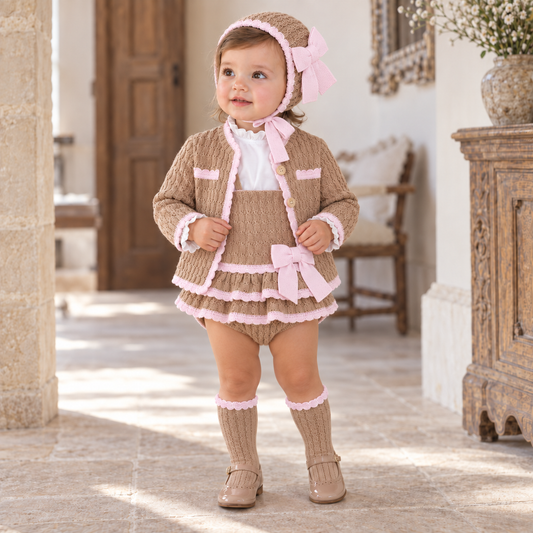 Young girl wearing the Rahigo camel and baby pink five-piece pinafore set with matching bonnet and knee-high socks
