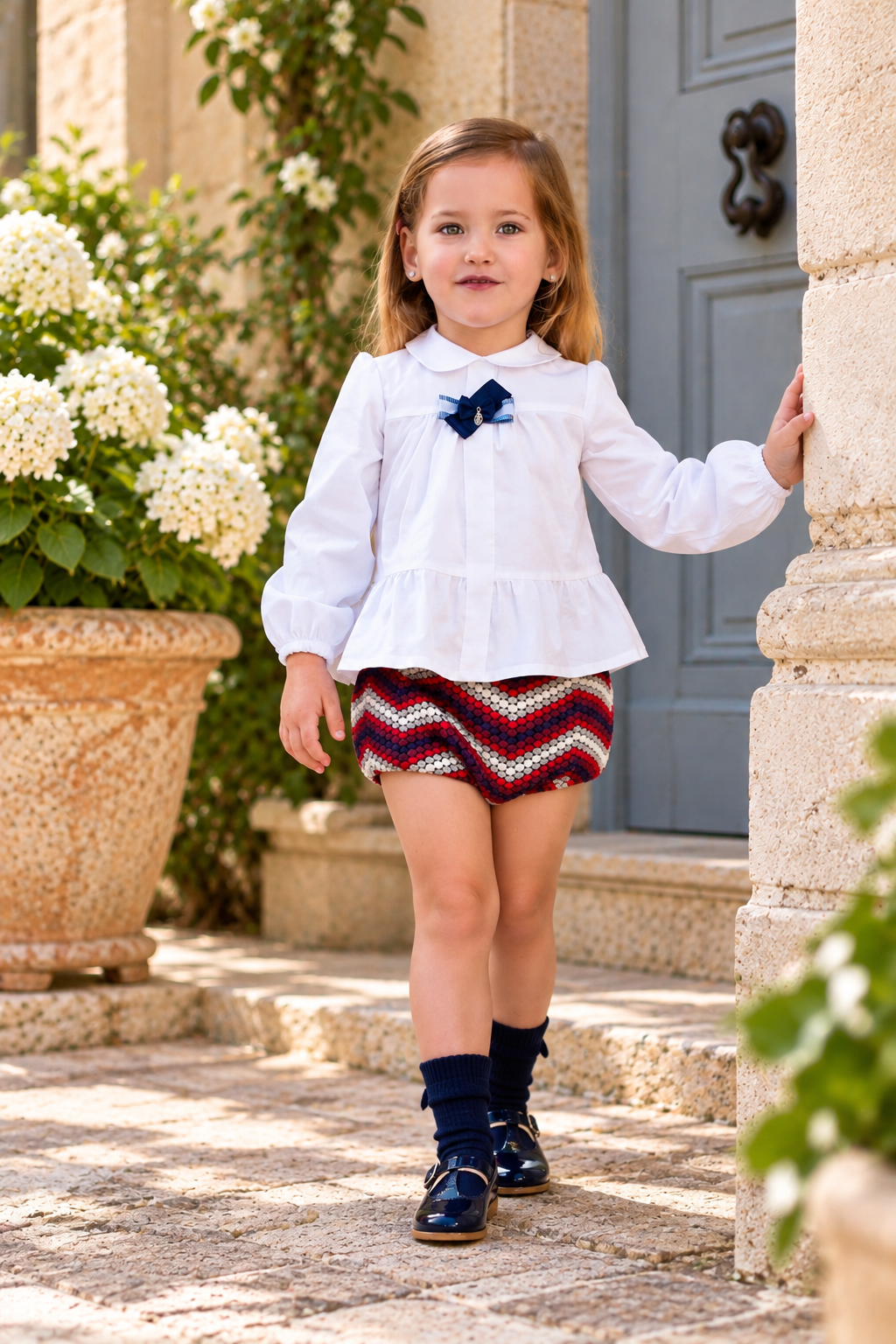 Rochy Bolas girls white blouse and red navy silver patterned jam pants in a sunlit Spanish courtyard