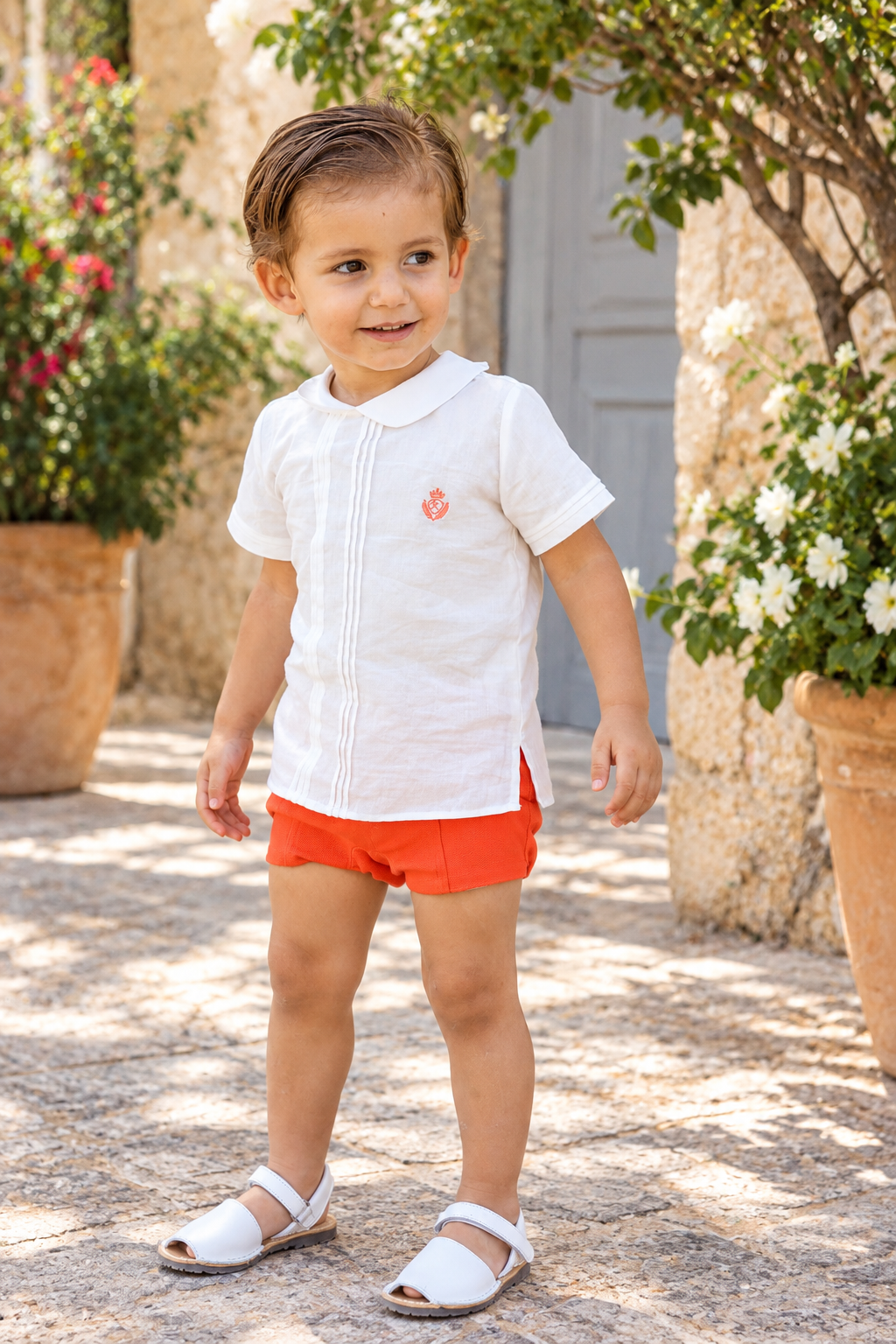 Rochy Coral Stripes boys white pleated shirt with coral crest and matching coral jam pants styled in a Spanish courtyard